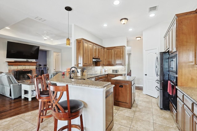 kitchen with sink, a breakfast bar area, light stone counters, kitchen peninsula, and black appliances