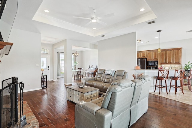 living room featuring ornamental molding, ceiling fan with notable chandelier, dark hardwood / wood-style flooring, and a tray ceiling