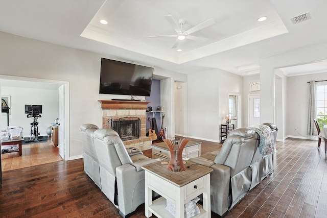 living room with dark wood-type flooring, ceiling fan, ornamental molding, and a tray ceiling