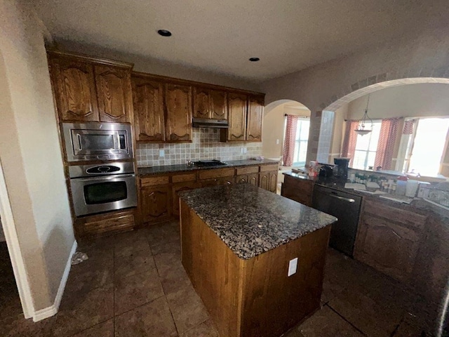 kitchen with tasteful backsplash, appliances with stainless steel finishes, a center island, and dark tile patterned flooring