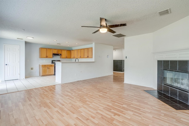 unfurnished living room with ceiling fan, light hardwood / wood-style flooring, a textured ceiling, and a fireplace