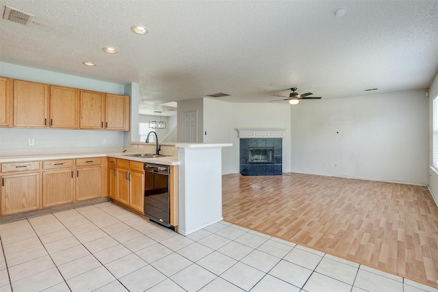 kitchen featuring light hardwood / wood-style flooring, a tile fireplace, dishwasher, sink, and kitchen peninsula