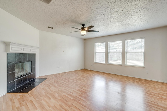 unfurnished living room with light wood-type flooring, ceiling fan, a textured ceiling, and a fireplace