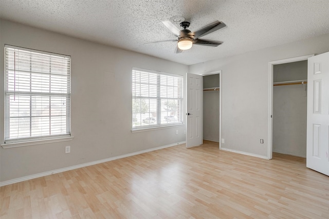 unfurnished bedroom featuring ceiling fan, multiple closets, a textured ceiling, and light hardwood / wood-style floors