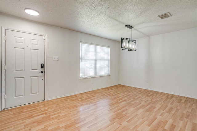 foyer with light hardwood / wood-style floors, a textured ceiling, and a chandelier