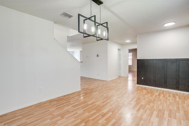 empty room featuring a textured ceiling, an inviting chandelier, and light hardwood / wood-style floors