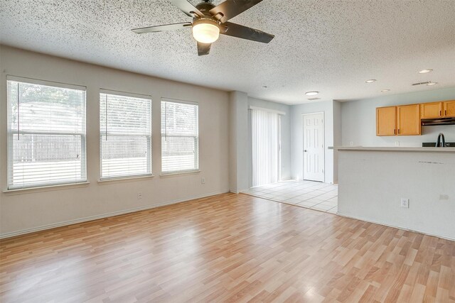 unfurnished living room featuring ceiling fan, plenty of natural light, light hardwood / wood-style flooring, and a textured ceiling