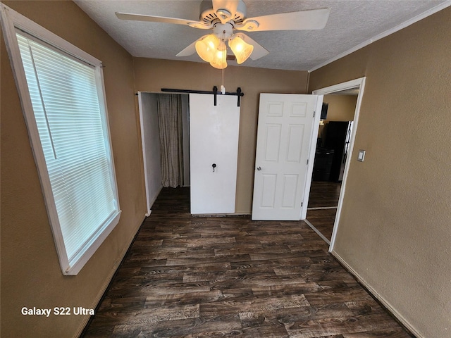 unfurnished bedroom with ceiling fan, a barn door, dark wood-type flooring, a textured ceiling, and a closet