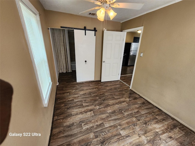 unfurnished bedroom with a barn door, fridge, dark wood-type flooring, and ceiling fan