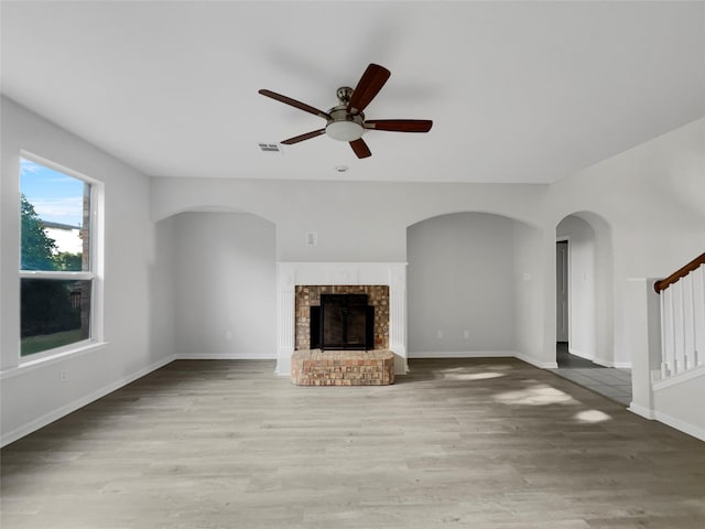 unfurnished living room featuring a brick fireplace, hardwood / wood-style floors, and ceiling fan