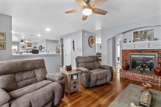 living room featuring a brick fireplace, hardwood / wood-style flooring, and ceiling fan