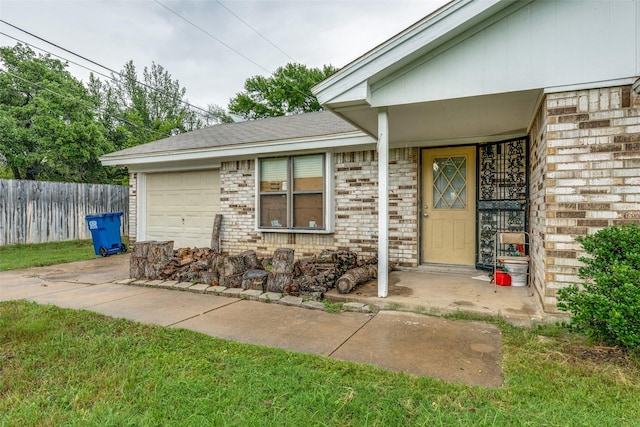 entrance to property with a garage, concrete driveway, brick siding, and fence