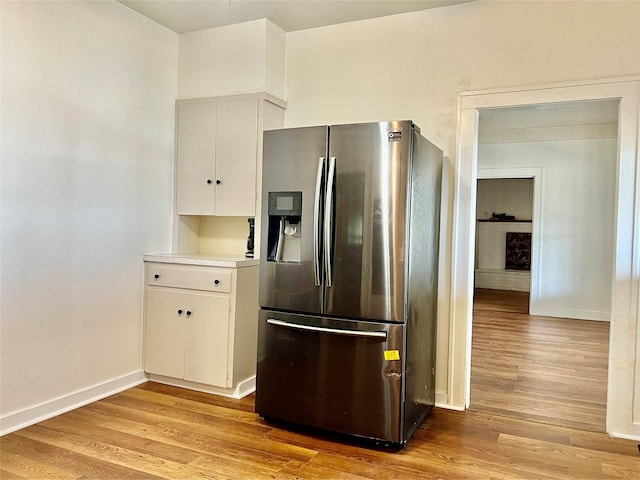 kitchen with light wood-type flooring, stainless steel fridge with ice dispenser, and white cabinets