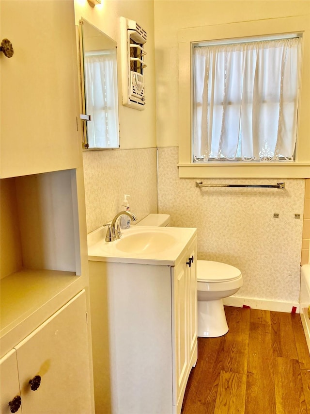 bathroom with wood-type flooring, a tub to relax in, vanity, and toilet