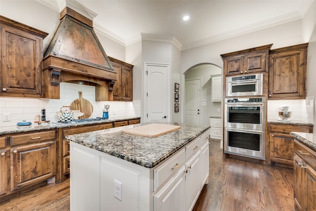 kitchen with wood-type flooring, backsplash, white cabinetry, crown molding, and premium range hood