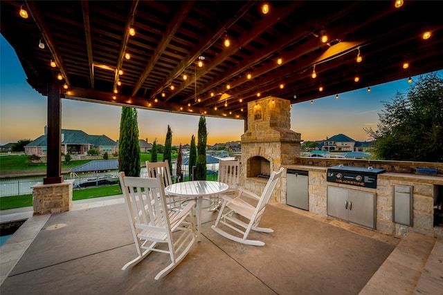 patio terrace at dusk featuring an outdoor stone fireplace and area for grilling