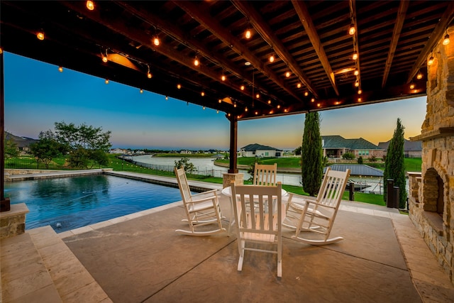 pool at dusk with a patio and a water view