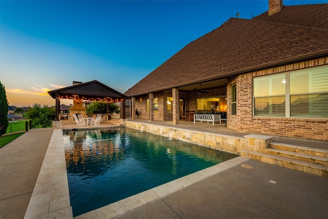 pool at dusk with a gazebo and a patio area