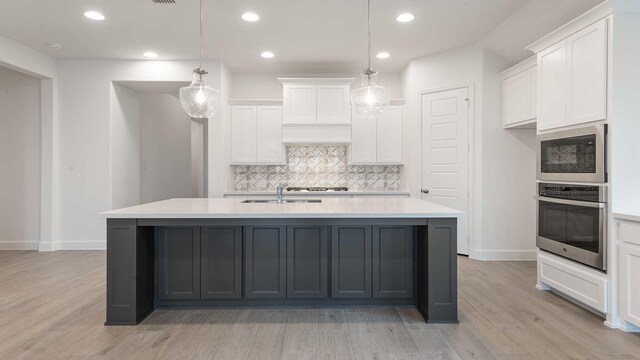 kitchen featuring pendant lighting, white cabinetry, stainless steel appliances, and a kitchen island with sink