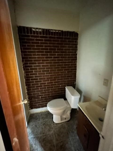 bathroom with vanity, brick wall, toilet, and tile patterned flooring