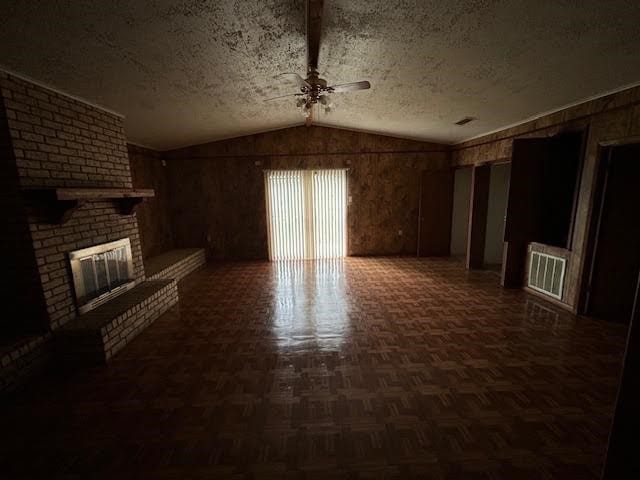 unfurnished living room with a fireplace, parquet floors, ceiling fan, vaulted ceiling, and brick wall