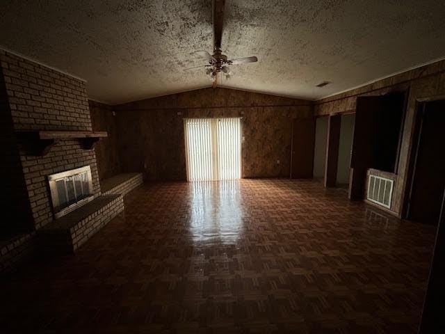 unfurnished living room featuring a textured ceiling, vaulted ceiling, a brick fireplace, and wood walls