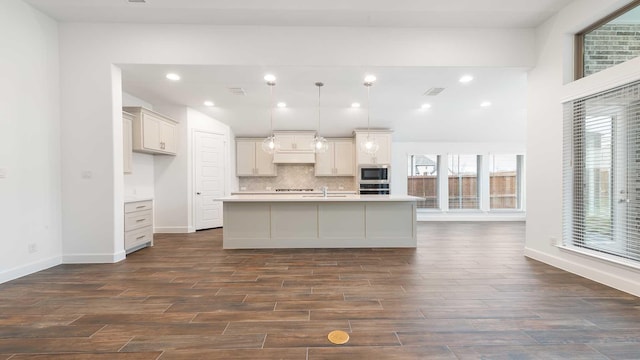 kitchen with dark wood-type flooring, pendant lighting, an island with sink, and stainless steel appliances