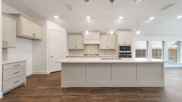 kitchen featuring sink, dark hardwood / wood-style floors, an island with sink, decorative light fixtures, and gas cooktop