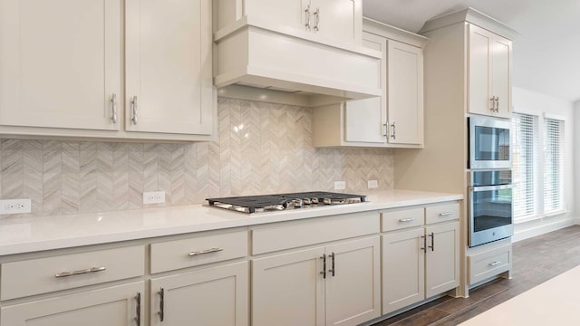 kitchen with decorative backsplash, appliances with stainless steel finishes, premium range hood, dark wood-type flooring, and white cabinets