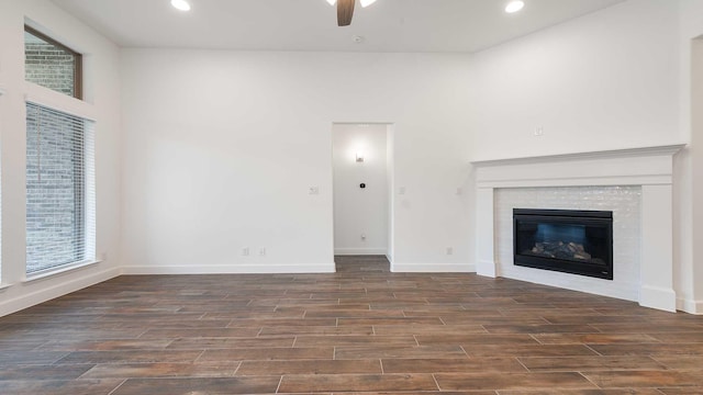 unfurnished living room featuring a tile fireplace, ceiling fan, and dark wood-type flooring