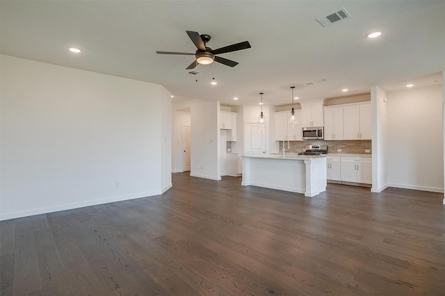 kitchen with decorative light fixtures, a center island with sink, stainless steel appliances, decorative backsplash, and white cabinets