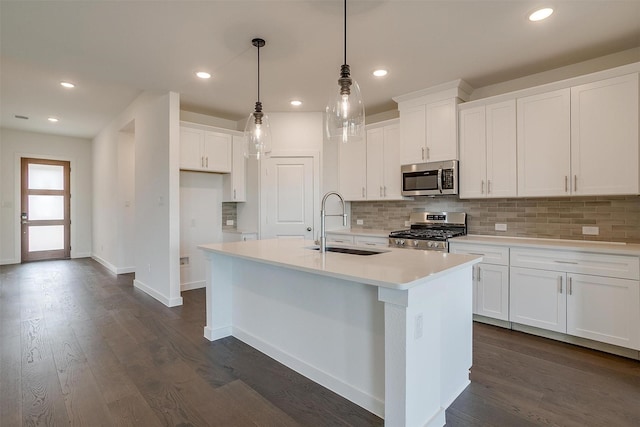 kitchen with sink, appliances with stainless steel finishes, white cabinetry, a center island with sink, and decorative light fixtures