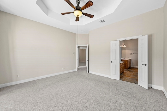 unfurnished bedroom with carpet floors, ensuite bathroom, a raised ceiling, and ceiling fan