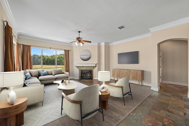 living room with ceiling fan, dark hardwood / wood-style floors, crown molding, and a tiled fireplace