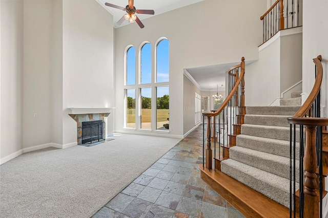 carpeted living room with ceiling fan with notable chandelier, ornamental molding, and a high ceiling