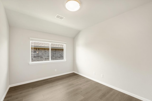 spare room with hardwood / wood-style floors and vaulted ceiling