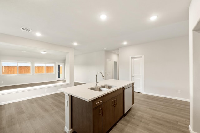 kitchen featuring dark brown cabinetry, sink, dishwasher, light hardwood / wood-style floors, and a kitchen island with sink