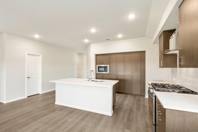 kitchen with sink, light wood-type flooring, built in microwave, an island with sink, and stainless steel range with gas stovetop