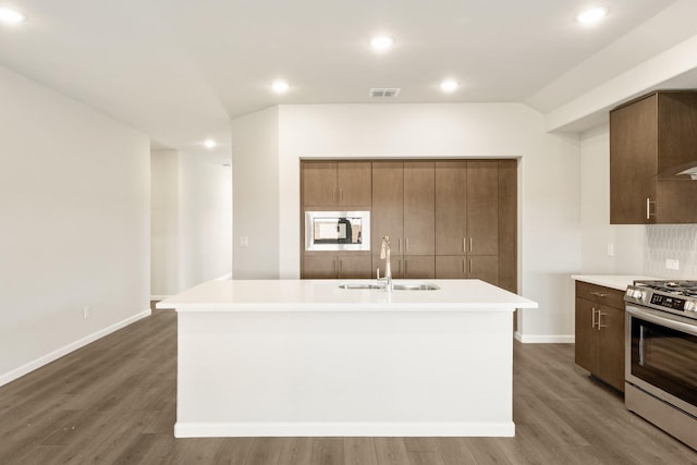 kitchen featuring sink, stainless steel range oven, an island with sink, and white microwave