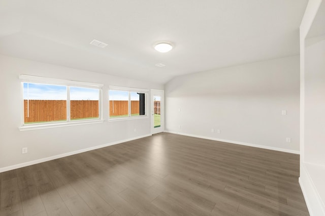 empty room with dark wood-type flooring, a wealth of natural light, and vaulted ceiling