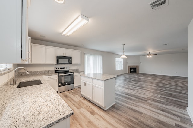 kitchen with a fireplace, light wood-type flooring, sink, a kitchen island, and stainless steel electric range oven