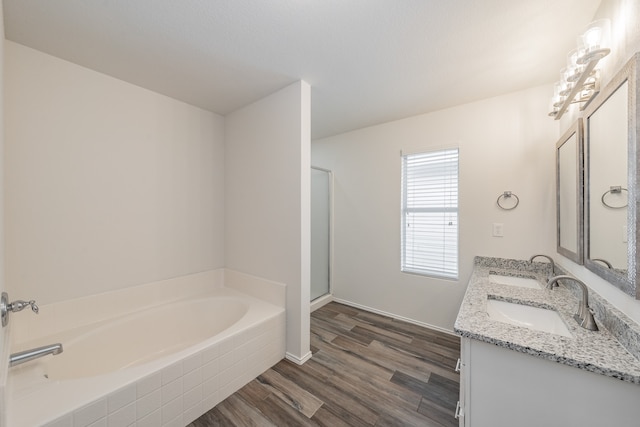 bathroom featuring a relaxing tiled tub, hardwood / wood-style flooring, and dual bowl vanity