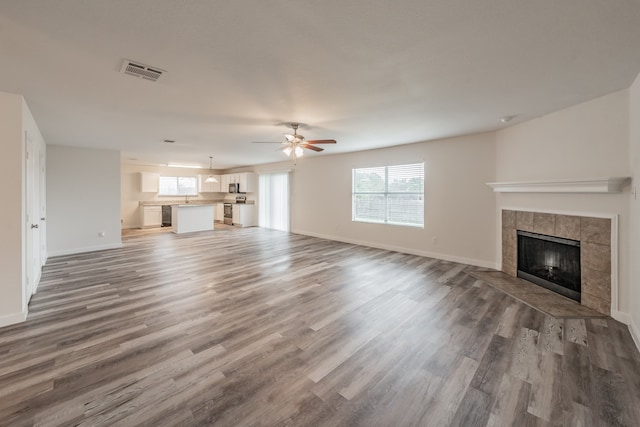 unfurnished living room featuring wood-type flooring, a tiled fireplace, sink, and ceiling fan