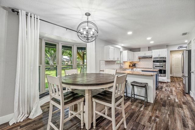 dining space featuring a textured ceiling, sink, dark wood-type flooring, and an inviting chandelier