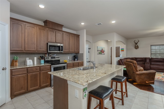 kitchen featuring a breakfast bar, an island with sink, sink, stainless steel appliances, and light stone countertops