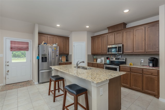 kitchen with sink, light stone counters, a center island with sink, stainless steel appliances, and decorative backsplash