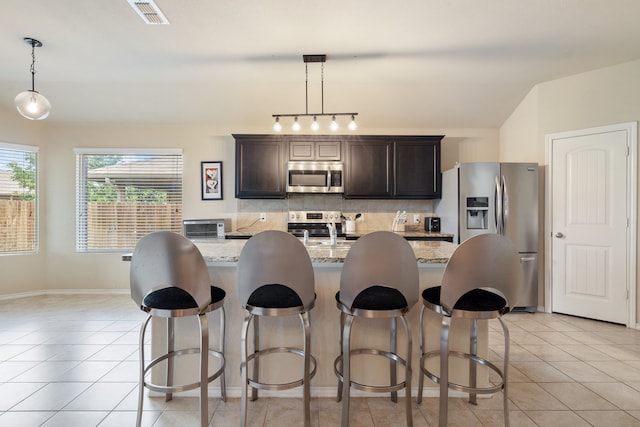 kitchen featuring light tile patterned flooring, appliances with stainless steel finishes, light stone countertops, tasteful backsplash, and hanging light fixtures