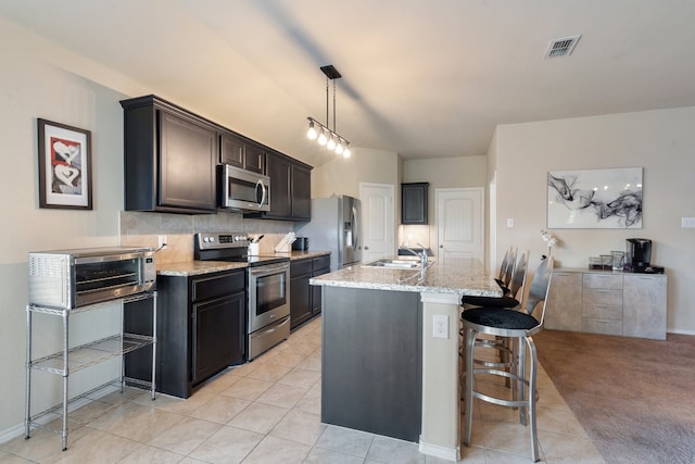 kitchen featuring appliances with stainless steel finishes, a kitchen bar, a kitchen island with sink, light colored carpet, and hanging light fixtures