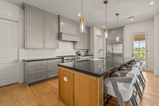 kitchen featuring decorative backsplash, high end appliances, a center island with sink, and light wood-type flooring