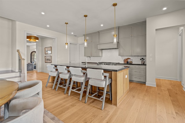 kitchen featuring light hardwood / wood-style flooring, tasteful backsplash, an island with sink, a kitchen breakfast bar, and gray cabinetry